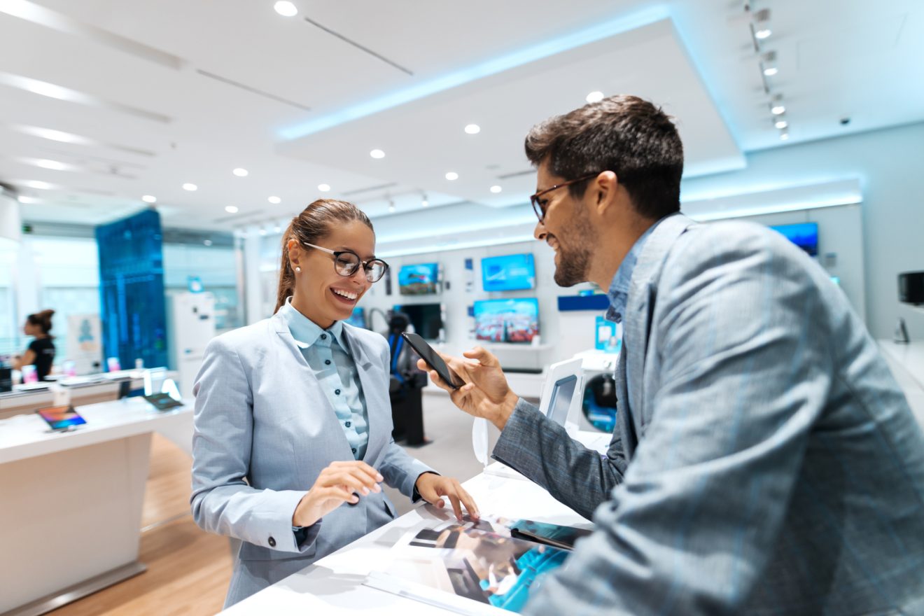 Young couple looking for new smart phone to buy. Woman looking at catalog while man holding smart phone.