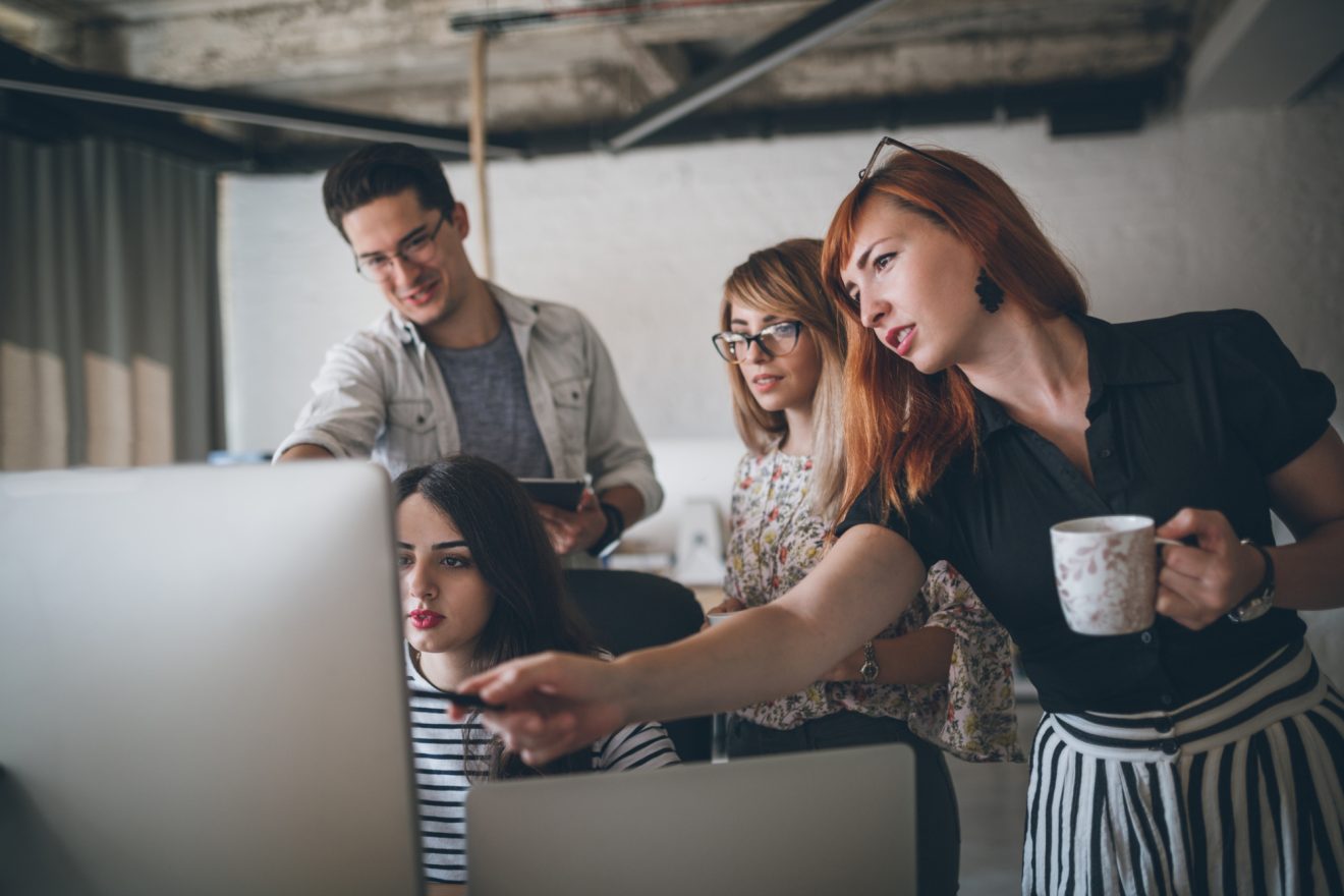 A group of people discuss work on one person's computer