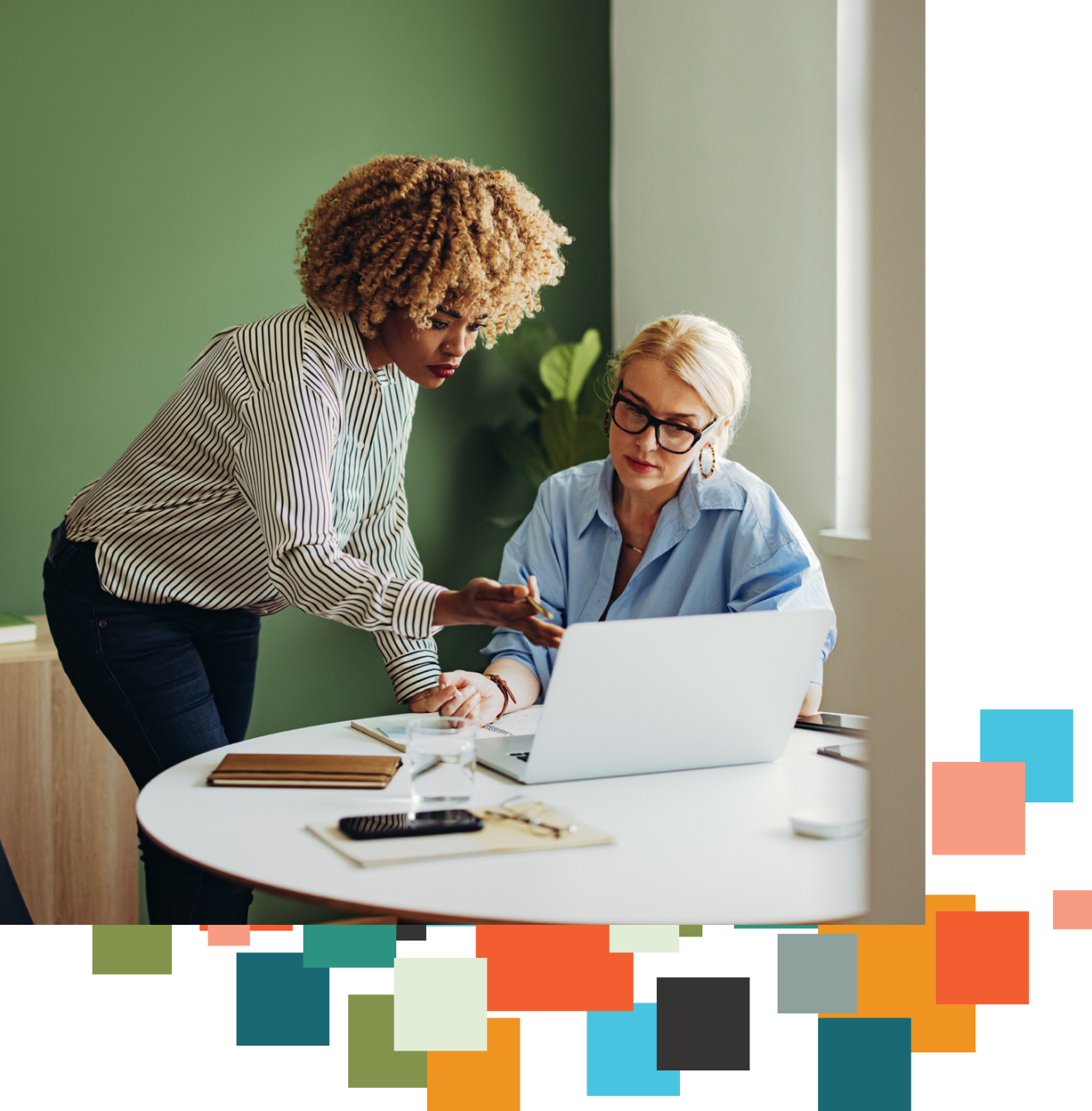 Two women talk together as one references a laptop